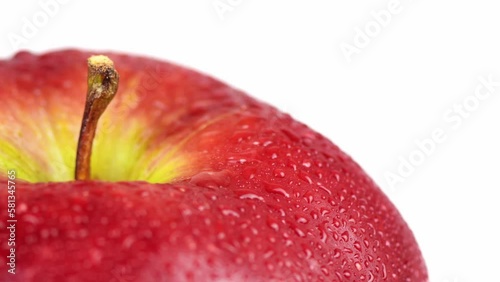 A Tempting Tempest. A Closeup View of a Rotating Red Apple with Water Droplets on White, positioned on the left.
