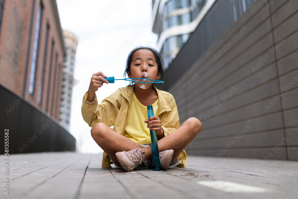 Little girl sitting in the city and blowing bubbles. Little girl sitting in the city and blowing bubbles.