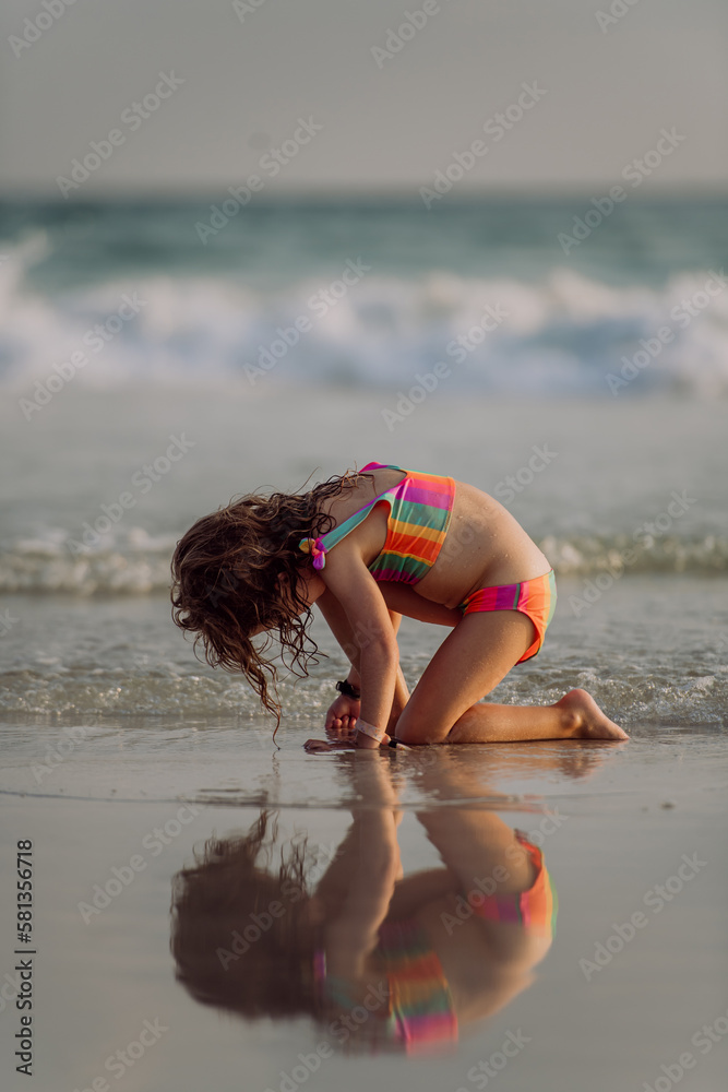 Naklejka premium Little girl looking for shells on the beach, enjoying exotic vacation.