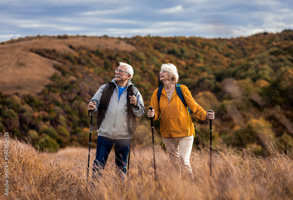 Active senior couple with backpacks hiking together in nature on autumn day.