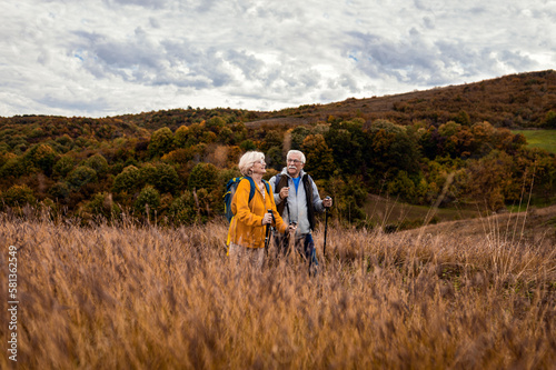 Active senior couple with backpacks hiking together in nature on autumn day.