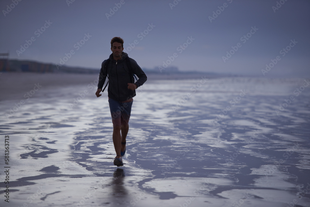 Starting the day with a jog on the beach. A young man jogging on the beach in the early morning. Starting the day with a jog on the beach. A young man jogging on the beach in the early morning.