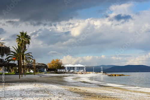 Empty beach off the season. No visitors walking on white sand, closed restaurant, cloudy sky and dark mountains on the background. Calm Mediterranean Sea on chilly sleepy day, Nea Makri, Greece.