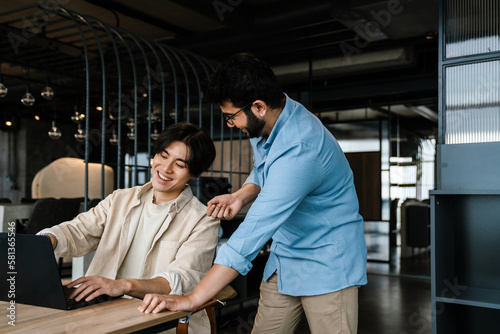 Two male colleagues working together on laptop computer in office