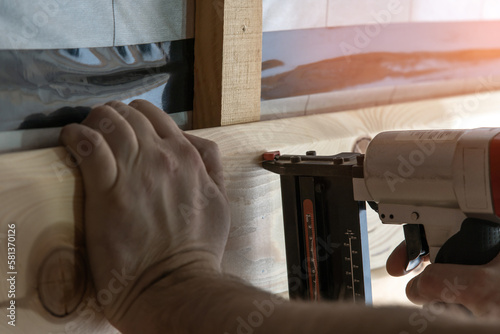 Cropped builder hands holding pneumatic nail gun, stapler for wooden board. Scoring, set up metal staples. Handiman work photo