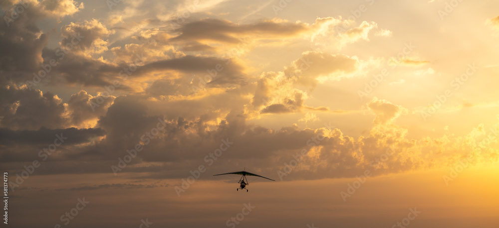 Naklejka premium Propeller plane flies in the sunset sky. Banner, A small private hang-glider in a cloudy sky.