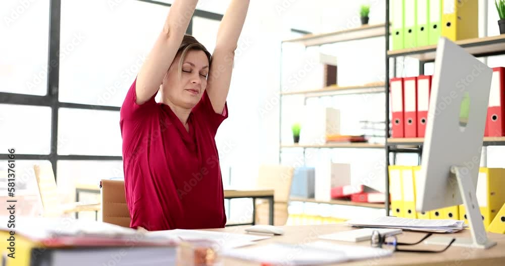 Woman stretches stretches her arms up at workplace in office Woman stretches stretches her arms up at workplace in office
