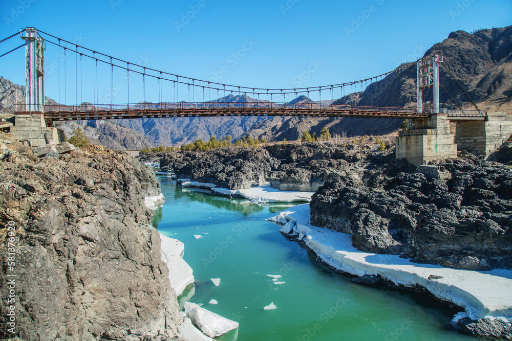 Bridge across the Katun River in the Altai Mountains, sunny day in early spring, travel and vacation - obrazy, fototapety, plakaty 