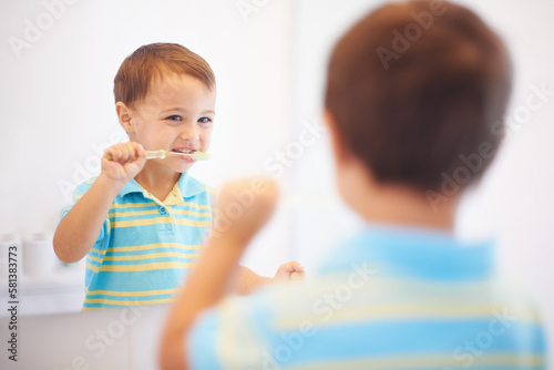 Hes learning healthy hygiene. a cute young boy brushing his teeth in a mirror.