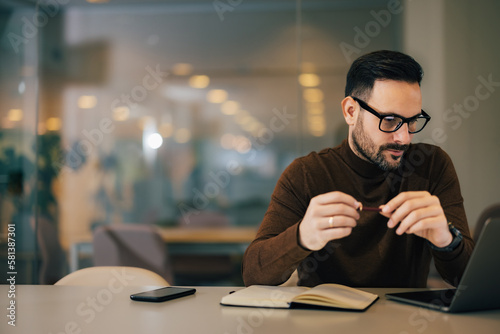 Smiling businessman reading an online book over the laptop, sitting at the office. photo