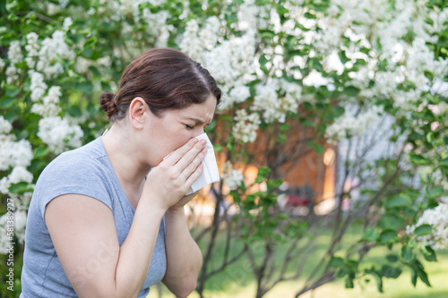 Caucasian woman suffers from allergies and blows her nose into a napkin while walking in the park. 