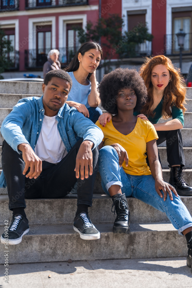 Obraz premium Portrait of happy multiethnic friends sitting on stairs in the city, young handsome models