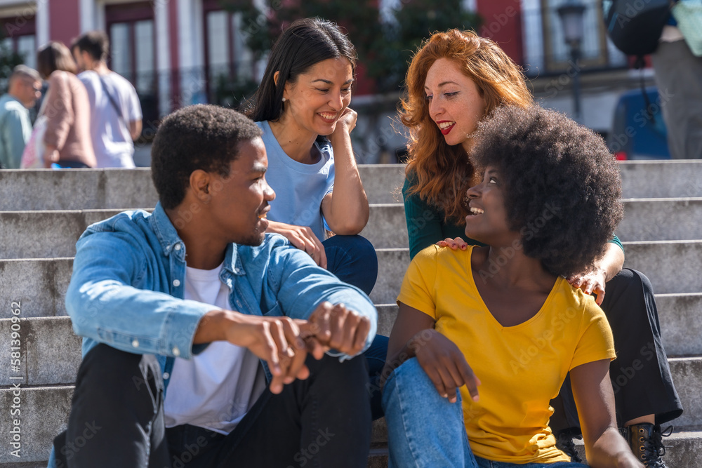 Fototapeta premium Happy multiethnic friends sitting on stairs in the city having fun, young handsome models
