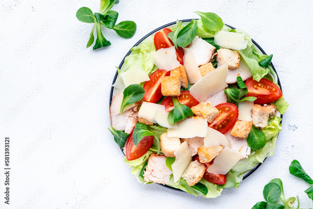 Caesar salad with chicken, iceberg salad, croutons, parmesan cheese and tomatoes with caesar dressing. White table background, top view Caesar salad with chicken, iceberg salad, croutons, parmesan cheese and tomatoes with caesar dressing. White table background, top view