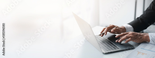 Person typing on laptop keyboard, businessman working on laptop, he is typing messages to colleagues and making financial information sheet to sum up the meeting.