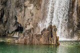 Partial view of lake, waterfall with water falling on sharp edged rock, Plitvice park, Croatia. Warm spring day to travel