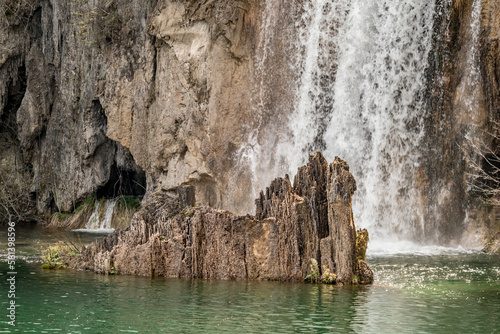 Partial view of lake, waterfall with water falling on sharp edged rock, Plitvice park, Croatia. Warm spring day to travel
