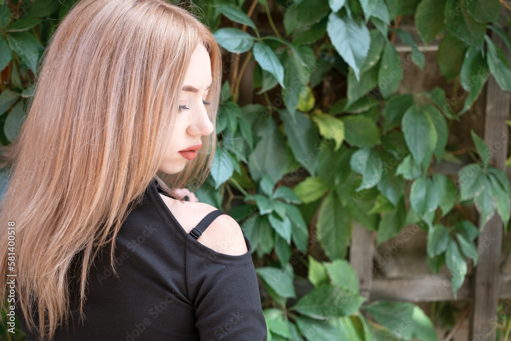 Portrait of attractive young blonde woman in black blouse, profile. Green plants background. Beautiful girl Portrait of attractive young blonde woman in black blouse, profile. Green plants background. Beautiful girl