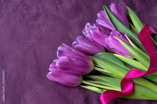 Flower bouquet of purple tulips with pink satin ribbon. Gift. Close up  copy space. Violet bedsheet as a background