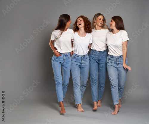 Four young caucasian women walking in blue jeans and white tshirt on grey background
