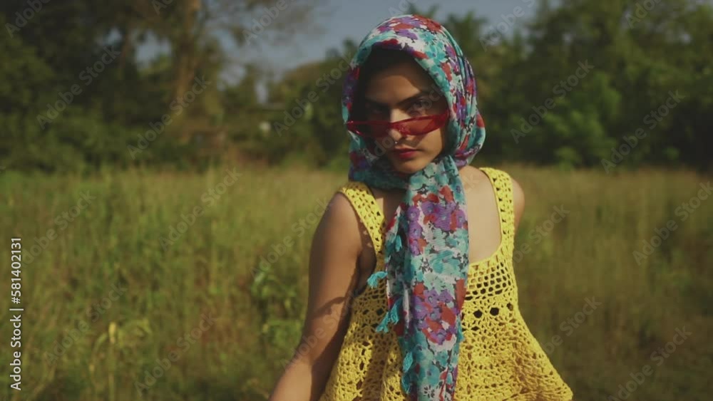 An attractive fashionable Asian female wearing a headscarf standing in a field surrounded by lush green grass An attractive fashionable Asian female wearing a headscarf standing in a field surrounded by lush green grass