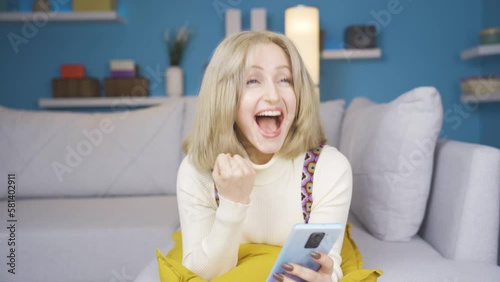 Young blonde woman looking at phone and rejoicing.
Woman lying on sofa looking at phone rejoicing. Blonde young woman.
