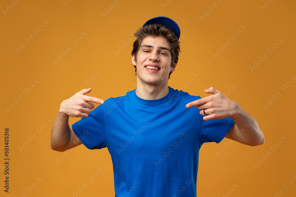 Young deliveryman pointing finger aside copy space on yellow background Young deliveryman pointing finger aside copy space on yellow background