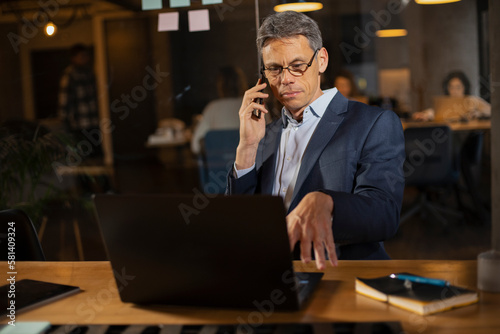  Businessman in office. Handsome man talking on phone at work.