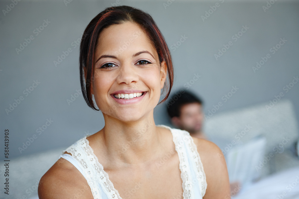 Feeling positive. Portrait of a smiling woman on the side of her bed with her boyfriend in the background. Feeling positive. Portrait of a smiling woman on the side of her bed with her boyfriend in the background.