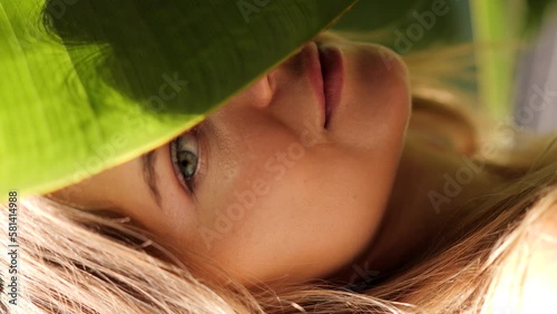  Face of young woman with clean skin with natural makeup among banana leaves