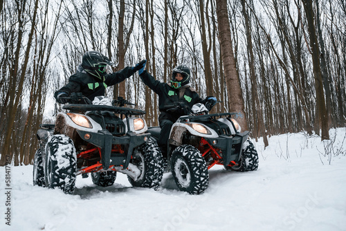 Making high five. Two people are riding ATV in the winter forest