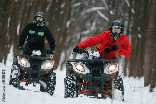 Conception of active recreation. Two people are riding ATV in the winter forest photo