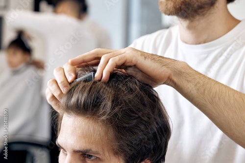 close-up, professional male hairstylist combing young customer's hair