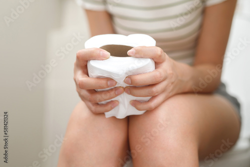 portrait of a woman suffers from diarrhea his stomach painful. ache and problem. hand hold tissue paper roll in front of toilet bowl. constipation in bathroom. Hygiene, health care concept.. photo