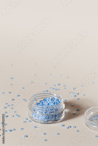 Elements for nails decor, blue stars in nail accessories box, stars for nail art in glass jar on beige background, copyspace. Creative beauty concept, pastel colors photo, visual content