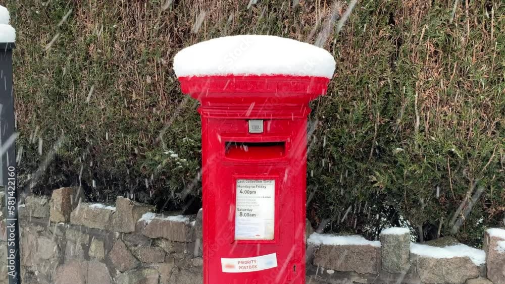 A British red post box for mail. It is snowing and the mailbox is covered in snow. A British red post box for mail. It is snowing and the mailbox is covered in snow.