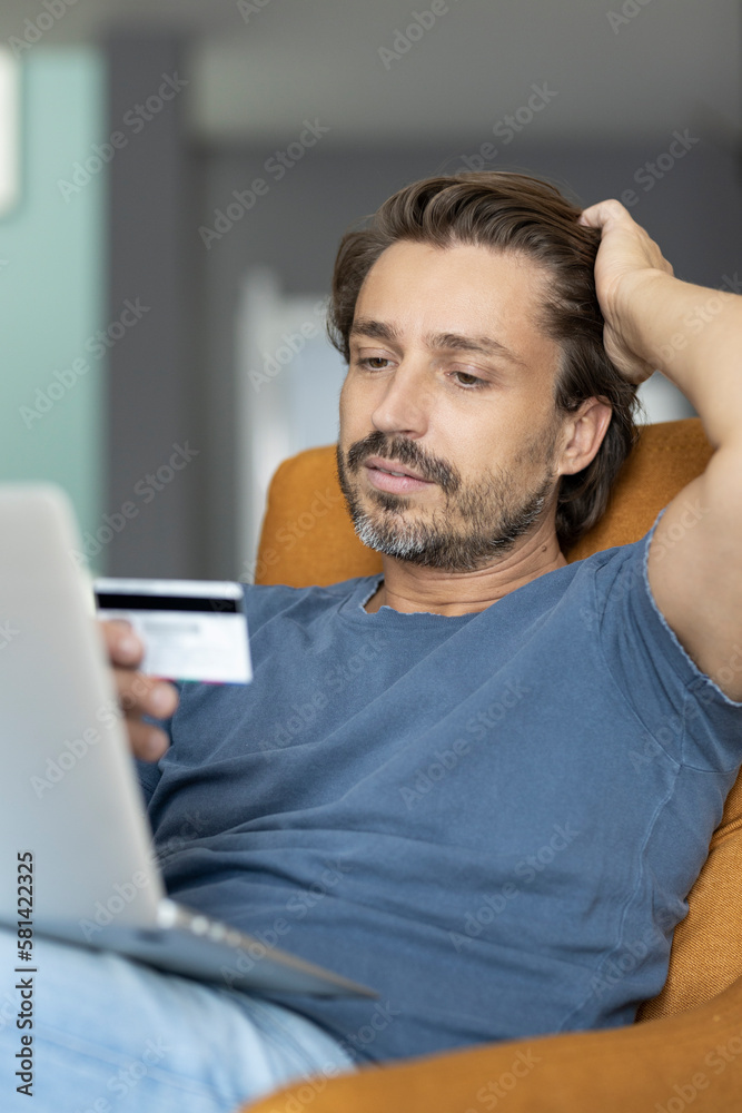 Man looking at his credit card information with his hand in the hair Man looking at his credit card information with his hand in the hair
