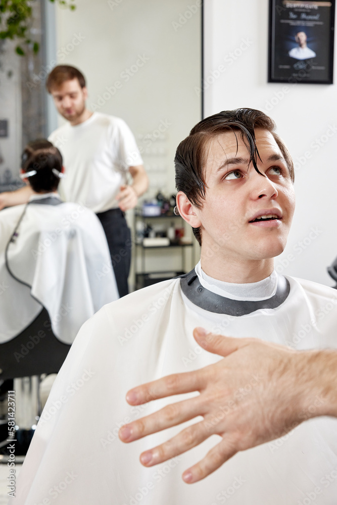 Fototapeta premium Barber talking to caucasian man while sitting in chair