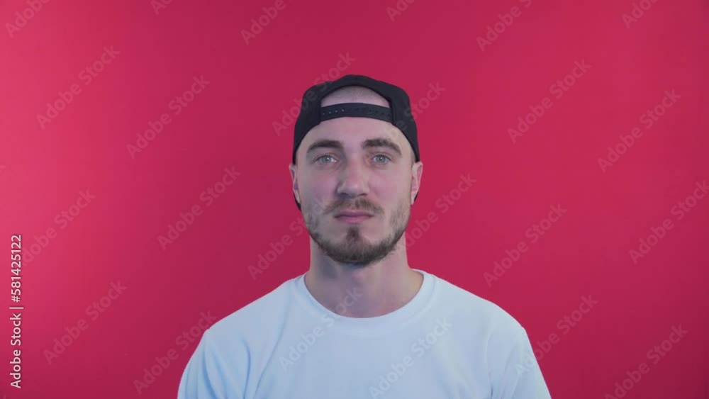 Male Attentive and Gazing. The Man Looks Stern and Serious Look at the Camera. Sighs, Shakes Head Slowly from Side to Side. A Man with a Baseball Cap on a Red background