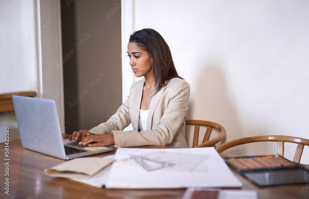 Setting up her own design website. A young woman typing on her laptop while sketches and pencils lie next to her on the desk. Setting up her own design website. A young woman typing on her laptop while sketches and pencils lie next to her on the desk.