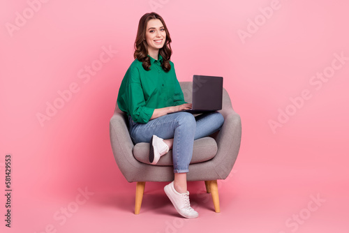 Full length photo of charming positive lady dressed green blouse sitting sofa typing emails modern device isolated pink color background