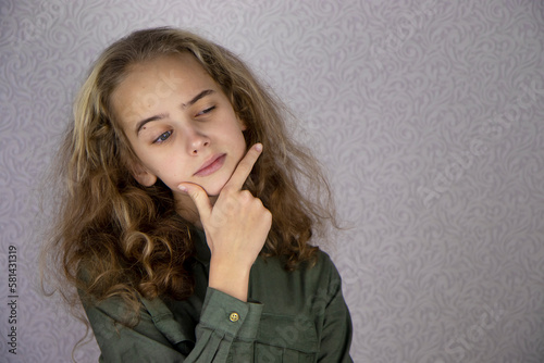 A cute teenage girl with blond hair thought about something, raising one eyebrow. Think by touching your face with your fingers.