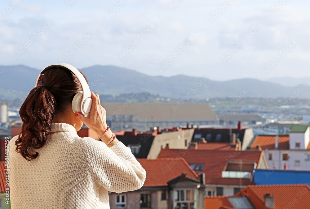 Adult woman putting on headphones to listen to music on a balcony