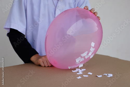 Closeup student do science experiment about static electricty from pink balloon and pieces of paper. Concept, Science project work activity. Learning by doing. Education.           