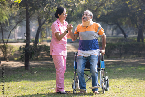Nurse talking to male senior patient on wheelchair with a neck brace at the park.