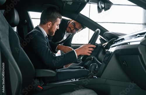 Side view. Man showing automobile interior to the customer