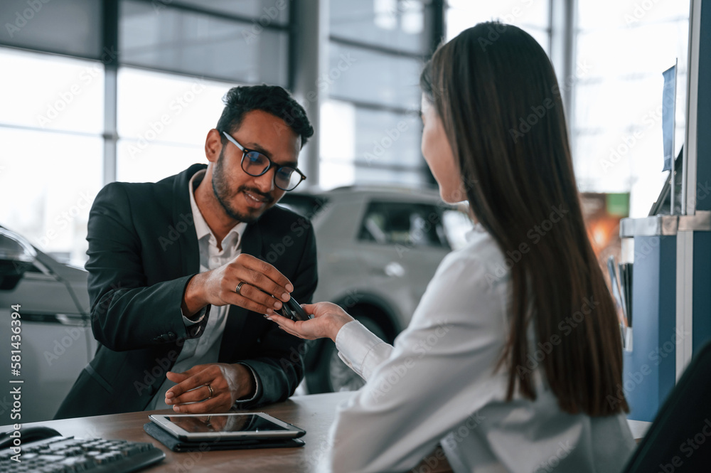 Woman is consulting man in the car showroom. Taking keys from the new automobile Woman is consulting man in the car showroom. Taking keys from the new automobile