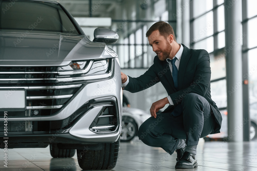Man in suit and tie is sitting and checking quality of the vehicle in the car showroom Man in suit and tie is sitting and checking quality of the vehicle in the car showroom