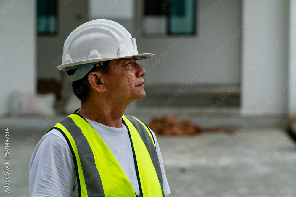 Asian construction worker standing and looking to the Right with construction site in background Asian construction worker standing and looking to the Right with construction site in background