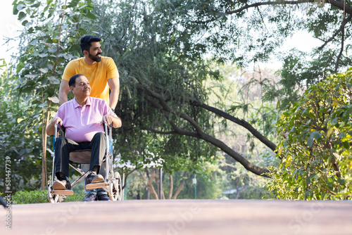 Young man assisting a senior man in a wheelchair at park